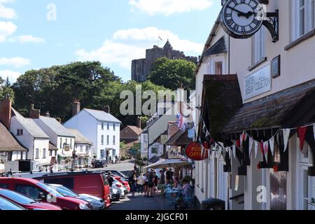 La rue animée de Dunster dans le Somerset lors d'une belle journée ensoleillée est surplombante par le magnifique château de Dunster. Il s'agit d'une propriété de National Trust Banque D'Images