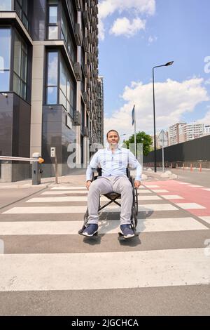 Homme handicapé en fauteuil roulant manuel sur le passage de zébré Banque D'Images