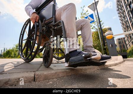 Homme handicapé en train de descendre le trottoir en fauteuil roulant manuel Banque D'Images