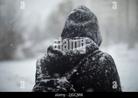 Homme dehors en chute de neige. Vêtements noirs dans la neige. Guy se trouve au centre de la ville. Blizzard dans la ville. Banque D'Images