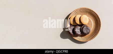 Sur la surface légère de la table de cuisine se trouve une assiette de papier brun avec de délicieux biscuits aux pépites de chocolat. Espace négatif à gauche. Banque D'Images