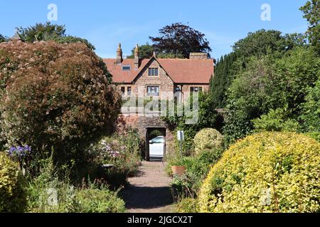 Les arbustes et les arbres de chaque côté d'un chemin de gravier mènent à une porte ouverte et à une grande maison. Le ciel est bleu et sans nuages Banque D'Images