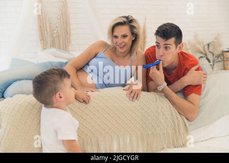 Jeune couple millénaire caucasien marié allongé sur leur lit et célébrant l'anniversaire de leur fils. Pavillon de fête soufflant pour papa. Photo de haute qualité Banque D'Images