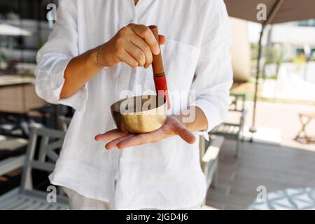 Les mains de l'homme court utilisant le bol de chant dans la thérapie de guérison sonore à l'extérieur, gros plan. Banque D'Images