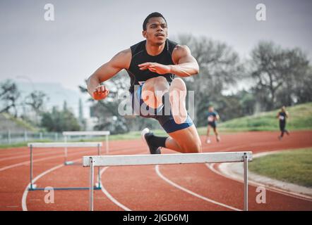 Naviguer facilement dans les obstacles. Tir en longueur d'un jeune athlète de sexe masculin pratiquant des haies sur une piste en plein air. Banque D'Images