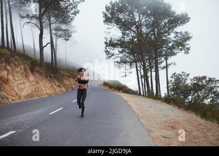 Jeune femme sportive qui court le matin sur une route de campagne. Jeune femme athlétique ayant une séance d'entraînement vigoureuse. Banque D'Images