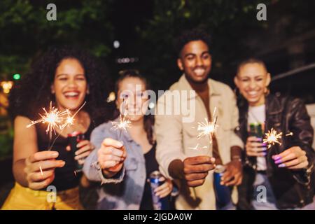 Des lumières Bengales pour les fêtes. Quatre jeunes heureux tenant leurs barboteurs la nuit. Groupe d'amis joyeux ayant un bon moment Banque D'Images