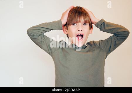 Je n'y crois pas. Studio photo d'un petit garçon mignon réagissant à quelque chose de surprenant et posant contre un mur. Banque D'Images