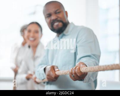 Tirez. Un beau homme d'affaires mature et ses collègues tirant sur une corde pendant le remorqueur de la guerre dans le bureau. Banque D'Images