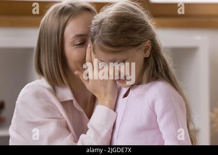 Bonne mère qui dit secret à sa fille, chuchote dans l'oreille des enfants Banque D'Images