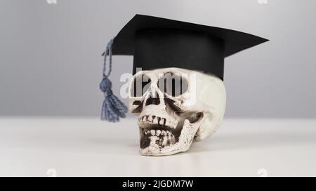 Crâne en plastique avec casquette universitaire sur fond blanc. Banque D'Images