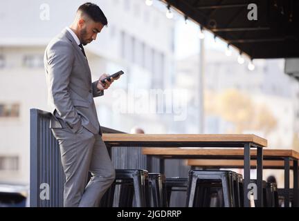 Un beau jeune homme d'affaires qui vérifie ses messages en attendant d'être assis dans un café Internet de la ville. Banque D'Images