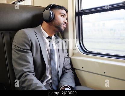 Assis avec ses pensées un peu. Un jeune homme d'affaires portant des écouteurs tout en regardant par la fenêtre sur un train pendant ses trajets. Banque D'Images