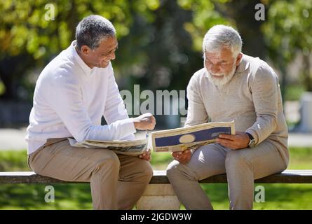 Avez-vous vu ce qui était dans le journal? Deux hommes âgés assis ensemble sur un banc dans le parc et lisant un journal. Banque D'Images