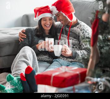 Rien ne peut briser notre lien. Un jeune couple qui boit du café tout en célébrant Noël à la maison. Banque D'Images