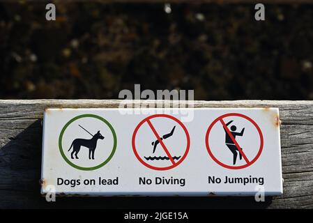 Corroder le panneau blanc sur un quai informant les gens que les chiens doivent être sur un plomb, et qu'aucun saut ou plongée dans l'eau n'est autorisé Banque D'Images