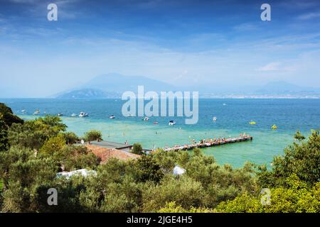 Vue sur le lac turquoise de Garde à Sirmione sur les oliviers, personnes méconnaissables bains de soleil et baignade Banque D'Images