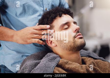 Rien de plus relaxant que le barber. Un beau jeune homme qui se fait soigné par un barber. Banque D'Images