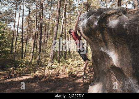 Le jeune homme sportif saute pour le coup de tête dans le célèbre et dur problème de bloc dyno appelé 'Cannon ball -7b'. Fontainbleau, France, Europe. Banque D'Images