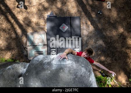 Le jeune homme sportif saute pour le coup de tête dans le célèbre et dur problème de bloc dyno appelé 'Cannon ball -7b'. Fontainbleau, France, Europe. Banque D'Images