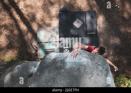 Le jeune homme sportif saute pour le coup de tête dans le célèbre et dur problème de bloc dyno appelé 'Cannon ball -7b'. Fontainbleau, France, Europe. Banque D'Images