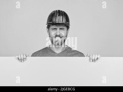 happy mature homme constructeur dans le casque derrière le papier jaune pour l'espace de copie, la publicité Banque D'Images
