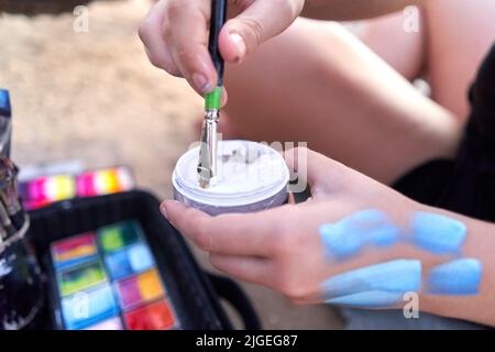 Artiste plongeant son pinceau dans la peinture assis sur une plage Banque D'Images