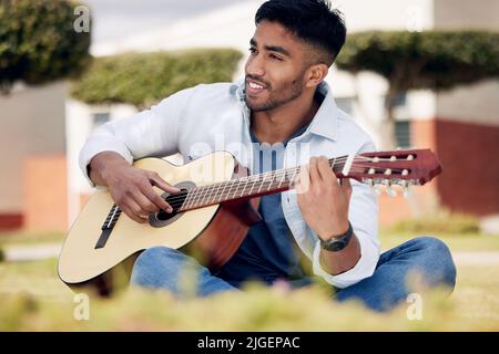 La bande-son de ma vie d'étudiant. Un jeune homme jouant de la guitare à l'extérieur à l'université. Banque D'Images