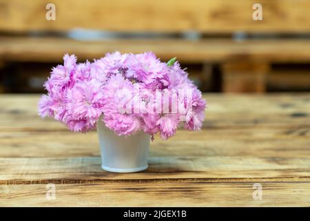 Œillets roses dans un seau blanc sur une table en bois. Place pour une inscription. Copier l'espace. Banque D'Images