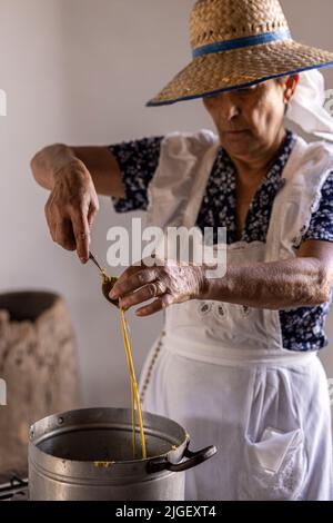 Chirche, Ténérife, 10 juillet 2022. Une femme faisant des bougies à partir de cire d'abeille en versant la cire fondue d'une cuillère sur une ficelle. Les villageois célèbrent la Día de tradiciones, jour des traditions dans le petit village de montagne où ils rendaient des scènes du style de vie rural vécu par leurs ancêtres en 1940s Banque D'Images