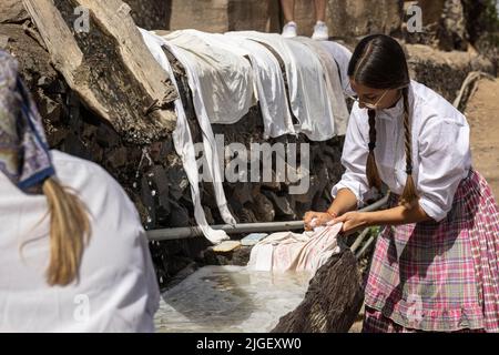 Chirche, Ténérife, 10 juillet 2022. Les jeunes filles lavant des vêtements dans un bac en bois à la station de lavage commune. Les villageois célèbrent la Día de tradiciones, jour des traditions dans le petit village de montagne où ils rendaient des scènes du style de vie rural vécu par leurs ancêtres en 1940s Banque D'Images