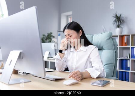 Épuisement au travail. Jeune femme asiatique fatiguée, femme d'affaires, gestionnaire, comptable, pigiste assis dans une chaise dans le bureau au bureau, travaille à la co Banque D'Images