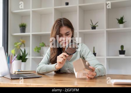 Femme heureuse main tenant la loupe et regardant le modèle de maison, sélection de maison, concept immobilier. Banque D'Images