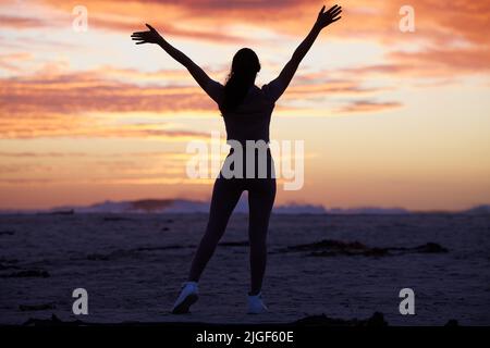 Il y a tant à apprécier dans la vie. Prise de vue en longueur d'une femme méconnaissable debout seule sur la plage avec ses bras levés. Banque D'Images