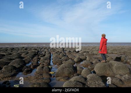 Femme en manteau rouge sur la plage de Hunstanton à marée basse Banque D'Images