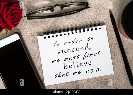 Citation motivationnelle sur un livre de notes sur table de marbre - pour réussir, nous devons d'abord croire que nous pouvons. Banque D'Images