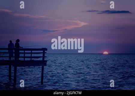 Les hommes sont silhouettés par le soleil couchant alors qu'ils pêchent, 1 juillet 2013, au quai de pêche de Cedar point sur la côte du golfe d'Alabama. Banque D'Images