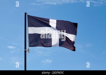 Drapeau de Saint Piran (Cornouailles) agitant au sommet de son poteau contre un ciel bleu. Banque D'Images