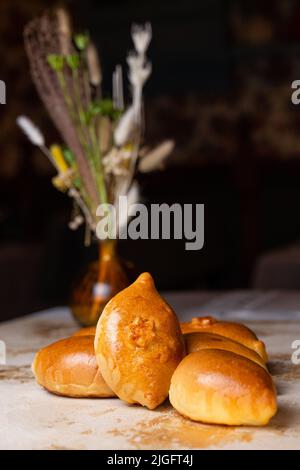 Tartes maison frites de grand-mère. Tartes avec pommes de terre sur la table avec fleurs. Banque D'Images