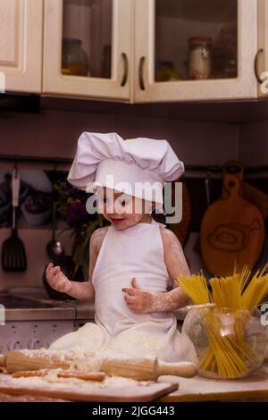 Un petit garçon dans les vêtements de cuisinier fait rouler la pâte avec un rouleau Banque D'Images