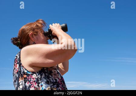 Femme hispanique mature regardant la distance à l'aide de jumelles à l'extérieur, un jour d'été. Concepts : aventure, voyage dans la nature, regarder dans le futur Banque D'Images