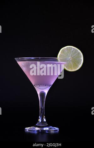 Cocktail cosmopolite, alcoolique avec glace et dans un grand verre avec une tranche de citron sur fond noir. Positionnement vertical. Banque D'Images