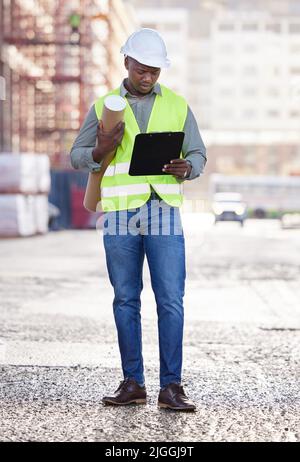 Garder un œil sur le processus. Photo en longueur d'un jeune ouvrier de la construction beau debout avec des plans et une planchette à pince sur un chantier de construction. Banque D'Images