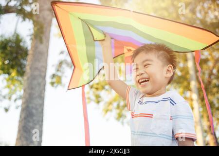 Un petit garçon asiatique heureux avec un cerf-volant pour s'envoler dans le parc au coucher du soleil en été Banque D'Images