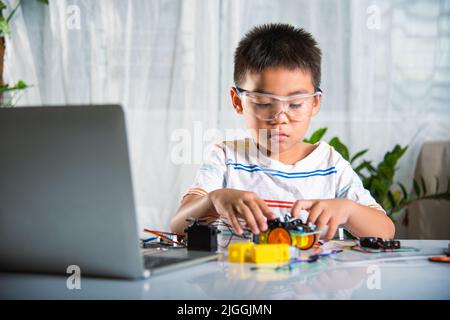 Enfant asiatique montage de roue dans Arduino robot de voiture devoirs, petit enfant essayant d'assembler la roue de construction à voiture jouet, créant la technologie électronique ai Banque D'Images