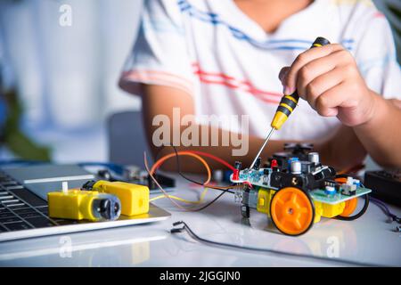 Un petit enfant serre l'écrou avec un tournevis pour assembler un jouet de voiture, un enfant asiatique assemblant le projet de travail de voiture robot Arduino à la maison, educatio Banque D'Images