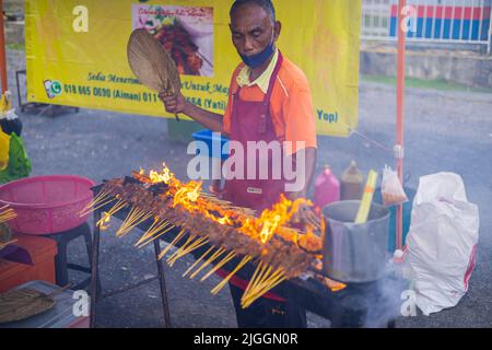 Kuala Lumpur, Malaisie - 21 juin 2022 : les barbecues de vieux hommes sont en feu ouvert sur un marché de nuit. Le plat sate est un plat grillé originaire d'Indonésie mais il est très bon Banque D'Images