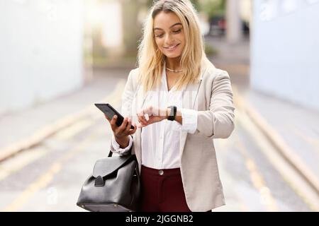 Regardez-vous l'heure. Une jeune femme d'affaires attirante qui vérifie l'heure tout en envoyant des SMS et en marchant dans la ville. Banque D'Images