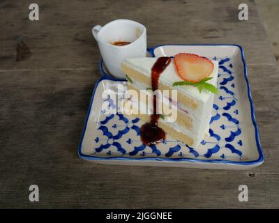 Tranche de fruits à la fraise et au kiwi avec sirop de couleur rouge et gâteau à la crème dans un plateau en céramique sur une table en bois gris, café expresso chaud dans une tasse blanche Banque D'Images