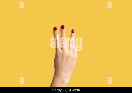 Vue latérale du profil gros plan de la main de femme avec manucure rouge montrant le numéro 3 trois avec les mains. Studio d'intérieur isolé sur fond jaune. Banque D'Images